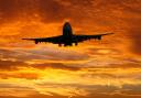 A plane flying in front of a sunset. Credit: Canva