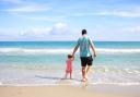 A father with his daughter walking on a beach (Canva)