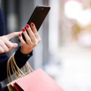 A woman on her phone holding shopping bags. Credit: Canva