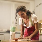 A woman using a rolling pin in her kitchen. Credit: Canva